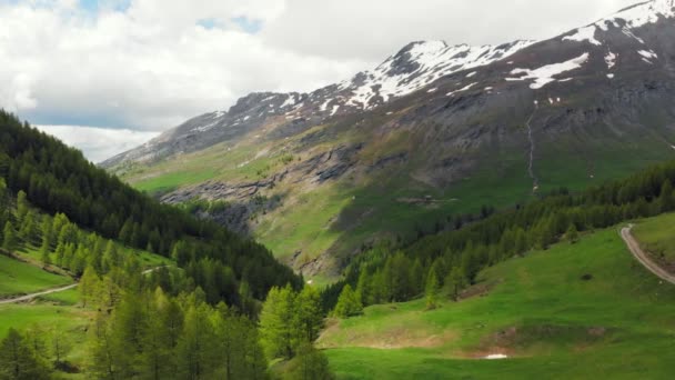 Ralenti aérien : survol de la vallée alpine, cascade pittoresque enneigée chaîne de montagnes et route spectaculaire sur les Alpes italiennes, voyage d'aventure en été .