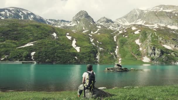 女子徒步旅行者坐在岩石上 看着风景 夏天的阿尔卑斯山上的蓝湖 白雪皑皑山脉 色调的形象 — 图库视频影像