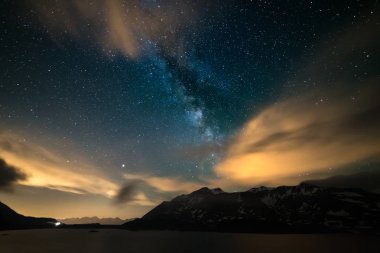 Astro gece gökyüzü, Samanyolu Alpler, fırtınalı gökyüzü, hareket bulutlar, karlı dağ ve göl üzerinde yıldız