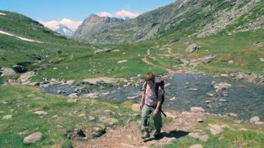 Pastoral dağ manzarası, mavi patika üzerinde hiking backpacker akan şelale akarsu. Alpler yaz maceralara. Ağır çekim.