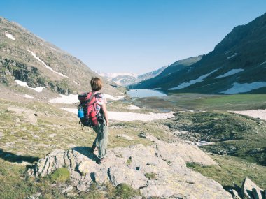 Bir kişi backpacker Alpler üzerinde yüksek rütbeli manzaraya bakarak. Expasive manzara, gün batımında pastoral görünümü. Arkadan Görünüş, tonlu görüntü.