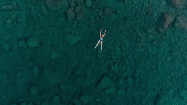 MOTION DE LENT AÉRIEN : femme flottant à la surface de l'eau bleue, nageant dans la mer Méditerranée transparente, vue du haut vers le bas, concept de vacances d'été 