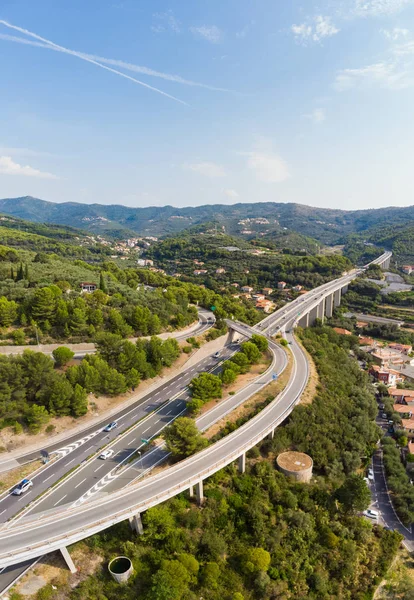 Aerial view of multiple lane highway crossing villages and forest hills (Autostrada dei Fiori - A10) Liguria Italy