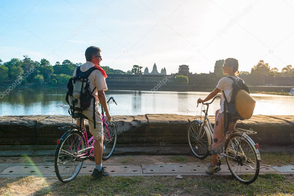 Tourist couple cycling in Angkor temple, Cambodia. Angkor Wat main facade reflected on water pond. Eco friendly tourism traveling.