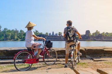 Turist çift Kamboçya Angkor tapınakta Bisiklete binme. Angkor Wat ana cephe su birikintisi üzerinde yansıtıyordu. Eko dostu turizm seyahat.