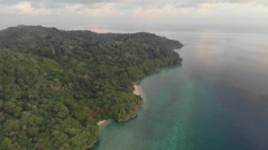 Hava: tropikal Hatta adası beyaz kum plaj Banda Adaları Maluku Endonezya yemyeşil orman turkuaz su mercan resif ilerler günbatımı gökyüzü üzerinde uçan. Yerli cinelike D-log renk profili