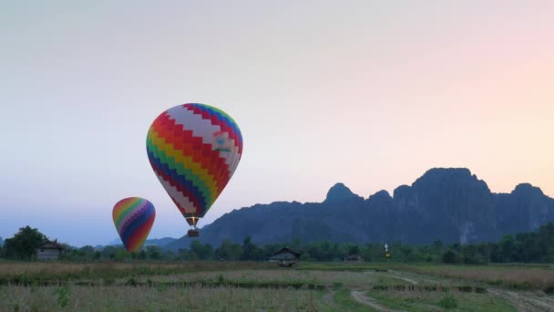 アジアのラオスのヴァンヴィエンバックパッカー旅行先に着陸する熱気球 観光活動風光明媚な崖岩の頂点夕日の風景 — ストック動画