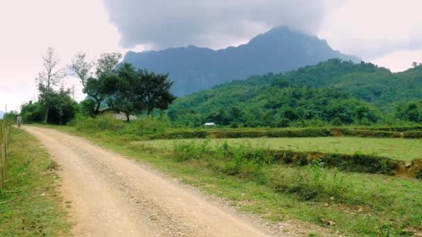 女性は ラオスの風光明媚な風景の中に未舗装の道路上でマウンテンバイクに乗るアジアの岩の頂点緑の谷のバックパッカーの旅行先 — ストック動画