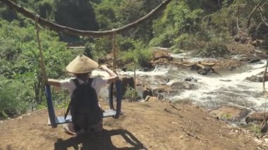 Geleneksel şapkalı kadın Banlung, Ratanakiri Kamboçya 'daki Kachanh Şelalesi' nde salıncakta sallanıyor.