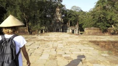 Yavaş çekim: Angkor'u ziyaret eden bir turist seyahat merkezi Kamboçya'yı harabeye çevirmektedir. Ormanda tapınağa yürüyen geleneksel şapkalı kadın, arka görüş