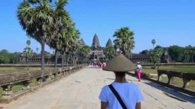 Angkor Wat seyahat hedef Kamboçya ziyaret eden bir turist. Tapınak harabelerine yürüyen geleneksel şapkalı kadın arka görüş.