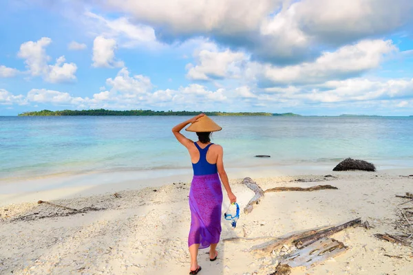 Mulher segurando máscara de snorkel na mão andando na praia tropical. Visão traseira, tradicional sul asiático chapéu turquesa mar dramático céu pessoas reais . — Fotografia de Stock