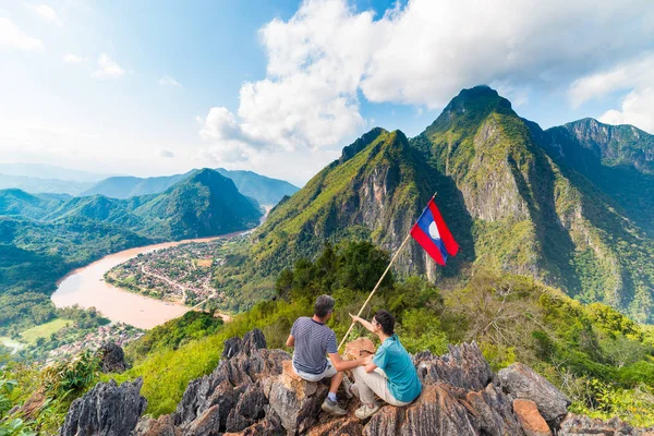 Pareja conquistando la cima de la montaña en Nong Khiaw vista panorámica sobre el valle del río Nam Ou Laos bandera nacional paisaje de montaña famoso destino de viaje en el sudeste de Asia — Foto de Stock
