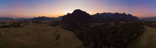 Aerial: Vang Vieng backpacker travel destination in Laos, Asia. Sunset over scenic cliffs and rock pinnacles, rice paddies valley, stunning landscape. — Stock Photo, Image