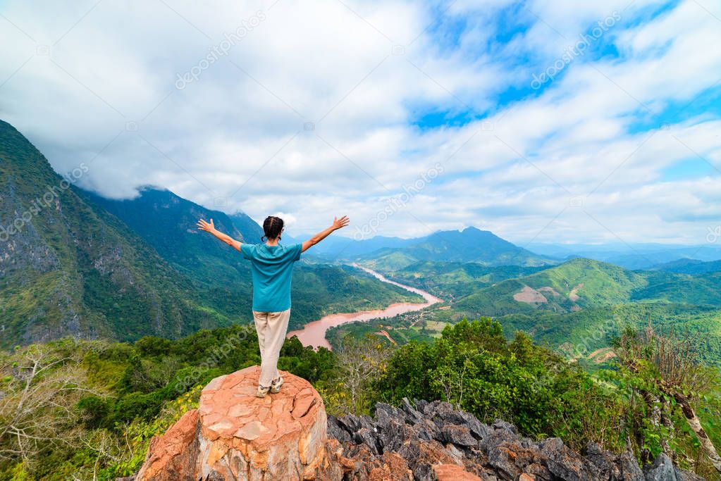 Woman with arms outstretched conquering mountain top at Nong Khiaw Nam Ou River valley Laos mature people traveling millenials concept travel destination in South East Asia