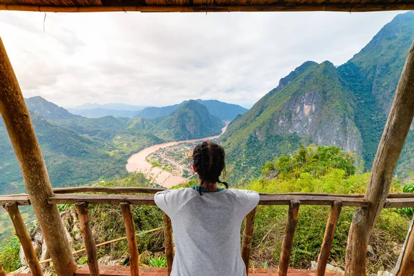 Женщина на деревянном балконе покоряющая вершину горы в долине реки Нонг Кхио Нам Оу Лаос зрелые люди путешествующие тысячелетия концепция путешествия назначения в Юго-Восточной Азии — стоковое фото