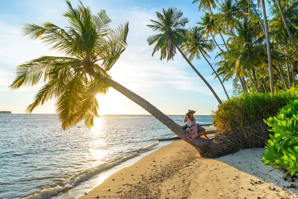 Femme avec chapeau asiatique traditionnel relaxant sur la plage tropicale assis sur le cocotier en contre-jour soleil couchant soleil éclater de vraies personnes. Indonésie, Îles Banyak, Sumatra destination voyage . — Photo