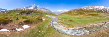 Alpler 'de yüksek dağ doruklarının havadan panoramik görünümü. İlkbahar sezonunda çayırlar arasında akan dere. Pastoral manzara, açık mavi gökyüzü, temiz kontamine olmayan çevre, su döngüsü.