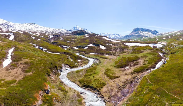 Alpler 'de yüksek dağ doruklarının havadan panoramik görünümü. İlkbahar sezonunda çayırlar arasında akan dere. Pastoral manzara, açık mavi gökyüzü, temiz kontamine olmayan çevre, su döngüsü. — Stok fotoğraf
