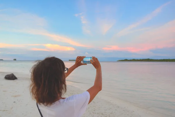 Mujer tomando fotos con teléfono inteligente del cielo romántico al atardecer en la playa de arena, vista trasera, personas reales que viajan por todo el mundo. Indonesia destino tropical, estilo de vida compartir concepto de redes sociales . —  Fotos de Stock