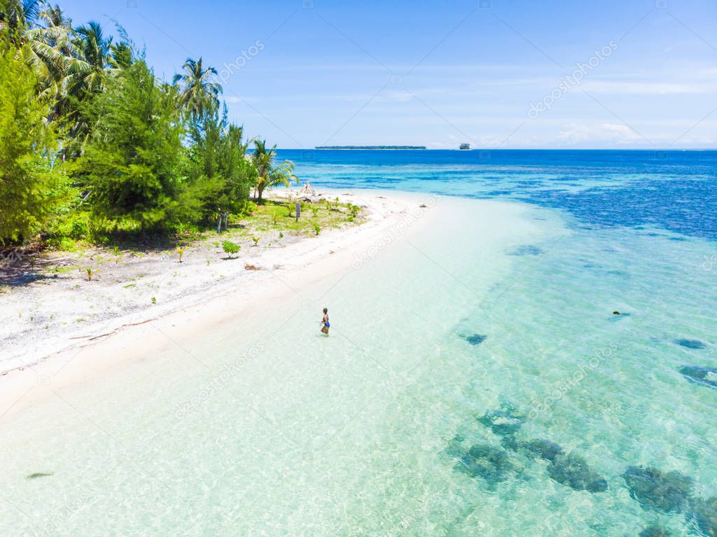 Aerial: Woman getting out of caribbean sea turquoise water tropical coral reef walking on white sand beach. Banyak Islands Sumatra Indonesia scenic travel destination