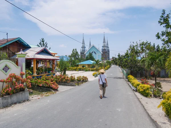 Vrouw met traditionele hoed wandelen in de straat van Ngurbloat, een kleine kleurrijke bloemrijke dorp met een enorme Christelijke Gotic stijl kerk in Kei Islands, Moluccas Indonesië. — Stockfoto