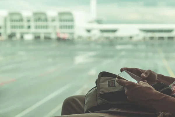 Usando el teléfono en el aeropuerto. Manos de mujer sosteniendo teléfono inteligente, aviones desenfocados y terminal. Imagen tonificada estilo vintage . —  Fotos de Stock