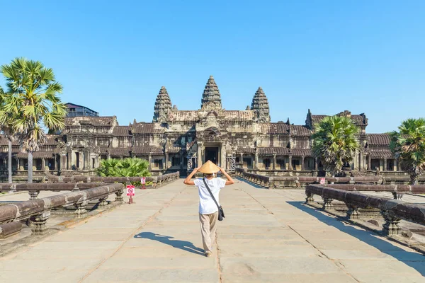 Un turista que visita las ruinas de Angkor Wat al amanecer, destino de viaje Camboya. Mujer con sombrero tradicional y brazos levantados, vista trasera, fachada principal y torres — Foto de Stock