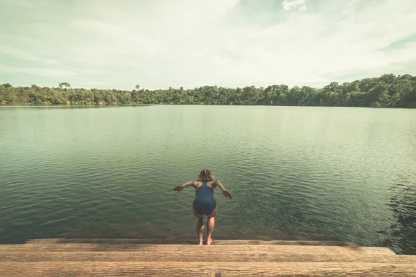 Mujer saltando en el agua del lago volcánico rodeado de bosque en Banlung, Camboya, destino de viaje. Tonificado estilo vintage — Foto de Stock