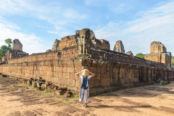 Gün doğumunda Angkor Wat harabelerini ziyaret eden bir turist, Rup Öncesi tapınağı, seyahat noktası Kamboçya. Geleneksel şapkalı ve kolları kaldıran kadın, arka görüş, fil heykeli