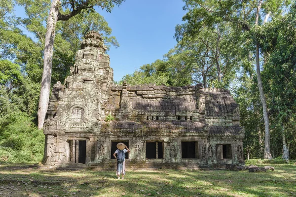 Um turista visitando Angkor ruínas em meio a selva, Angkor Wat templo complexo, destino de viagem Camboja. Mulher com chapéu tradicional, vista traseira . Imagens De Bancos De Imagens