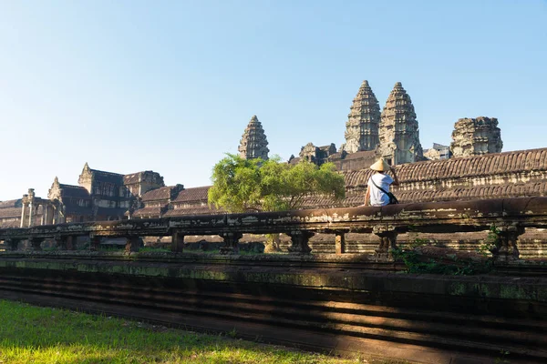 Un turista que visita las ruinas de Angkor en medio de la selva, complejo de templos de Angkor Wat, destino de viaje Camboya. Mujer con sombrero tradicional, vista trasera . — Foto de Stock