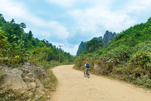 Mujer montando bicicleta de montaña en el camino de tierra en paisaje escénico alrededor de Vang Vieng destino de viaje mochilero en Laos Asia pináculos de roca verde valle — Foto de Stock