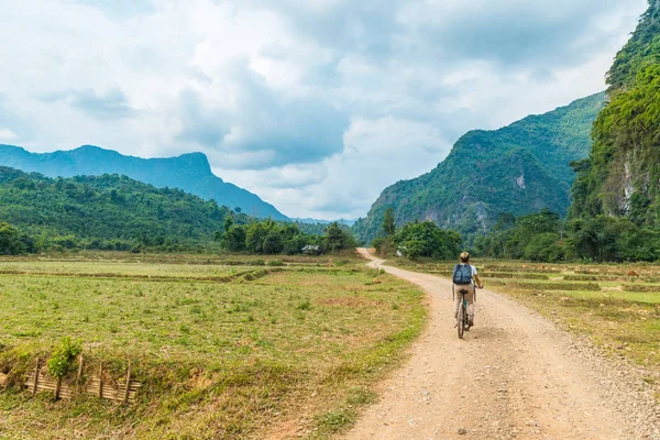 Donna in sella mountain bike su strada sterrata in paesaggio panoramico intorno a Vang Vieng zaino in spalla destinazione di viaggio in Laos Asia roccia pinnacoli verde valle — Foto Stock