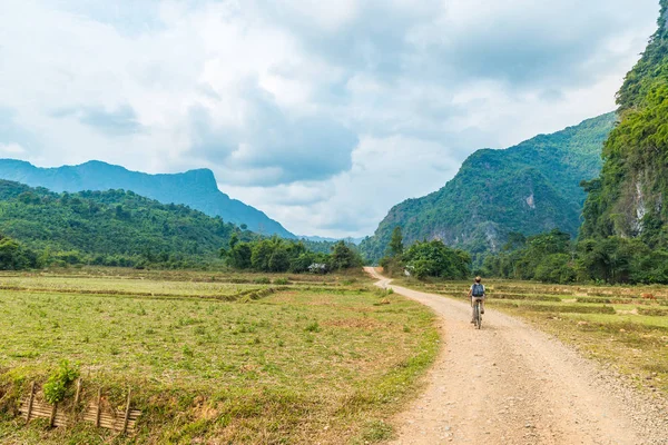 Mulher montando bicicleta de montanha na estrada de terra na paisagem cênica em torno de Vang Vieng destino de viagem mochileiro no Laos Ásia pináculos de rocha vale verde — Fotografia de Stock