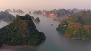 Aerial: unique flying over Ha Long Bay and Cat Ba island at sunset, famous tourism destination in Vietnam. Scenic sky with clouds, limestone rock peaks in the sea at the horizon.