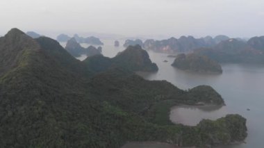 Aerial: unique flying over Ha Long Bay and Cat Ba island at sunset, famous tourism destination in Vietnam. Scenic sky with clouds, limestone rock peaks in the sea, d-log flat color profile