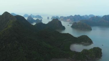 Aerial: unique flying over Ha Long Bay and Cat Ba island at sunset, famous tourism destination in Vietnam. Scenic sky with clouds, limestone rock peaks in the sea, d-log flat color profile