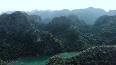 Hava: Ha Long Körfezi kaya tepeleri üzerinde uçmak, Vietnam 'daki ünlü seyahat noktaları. Tekneler ve kanodaki turistler eşsiz kireçtaşı zirveleri, denizdeki adalar, manzaralı körfezler ve yeşil orman arasında