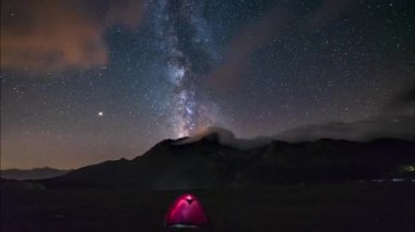 Samanyolu 'nun Zaman Hızı ve yıldızlı gökyüzü yaz mevsiminde görkemli İtalyan Fransız Alpleri üzerinde dönüyor. Ön planda aydınlatılmış kamp çadırı.