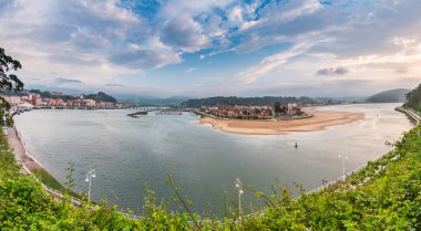 İspanya 'nın Asturias kentindeki Ribadesella kıyı kasabasında, kumlu nehir ağızları denize doğru kıvrılıyor, renkli evler, arka planda dağlar, yukarıda bulutlu gökyüzü, kültür ve doğa harmanlanıyor..