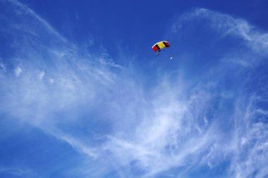Kırmızı sarı paraşüt gölgelik ve dumanlı bulutlar arka planı ve parlak mavi gökyüzü karşı tandem'ın skydivers. Uçuş ve iniş prepearing tandem ustası yolcu ile.