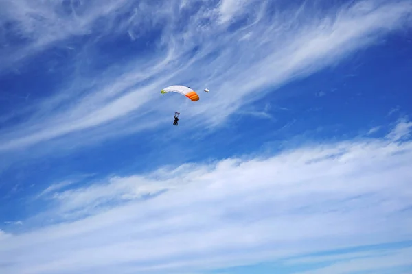 Parlak beyaz paraşüt gölgelik ve tandem'ın skydivers sıradışı bulutlar ve mavi gökyüzü arka planı. Uçuş ve iniş prepearing tandem ustası yolcu ile.
