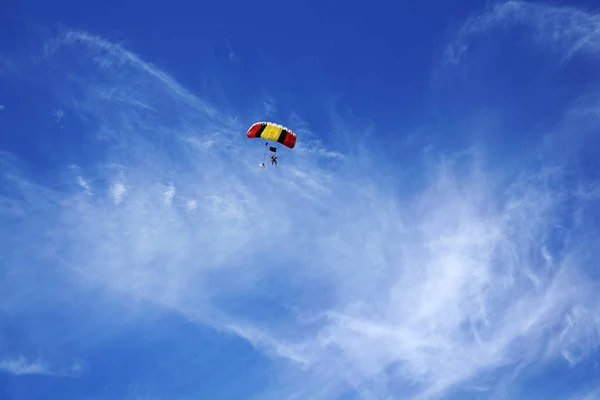 Çok renkli kırmızı-sarı siyah paraşüt gölgelik ve skydivers bir bulanık lighty arka planı mavi gökyüzü ve bulutlar. Uçuş ve iniş prepearing tandem ustası yolcu ile.