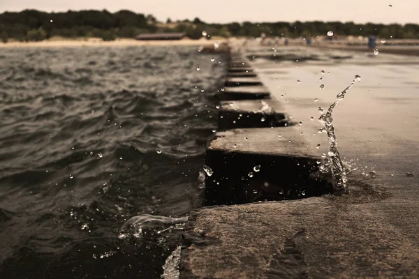 Dalga sıçrama metal sınır elemanları ile iskele iskele üzerinde. Su sıçramasına bulutlu havalarda. Splash iskele üzerinde dondu. ABD, Michigan Eyaleti, Michigan Gölü.