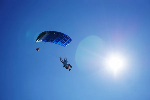 Skydiver with a blue parachute close up under sunshine