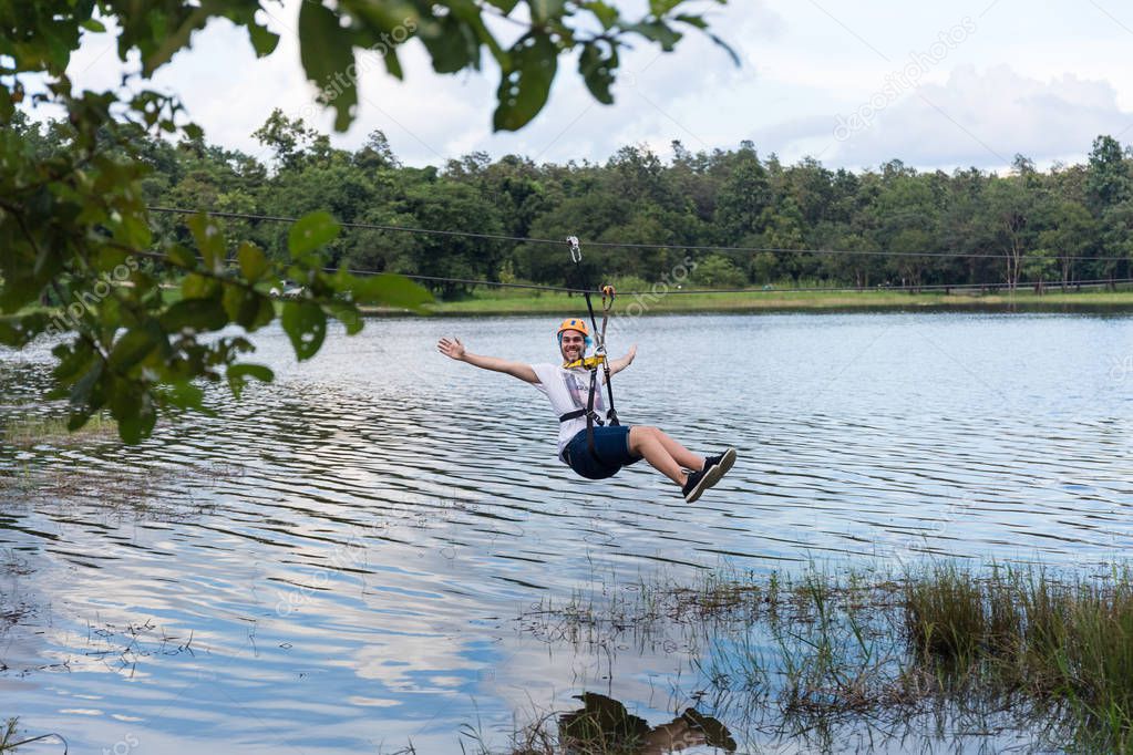Young man crossing a lake in zip line