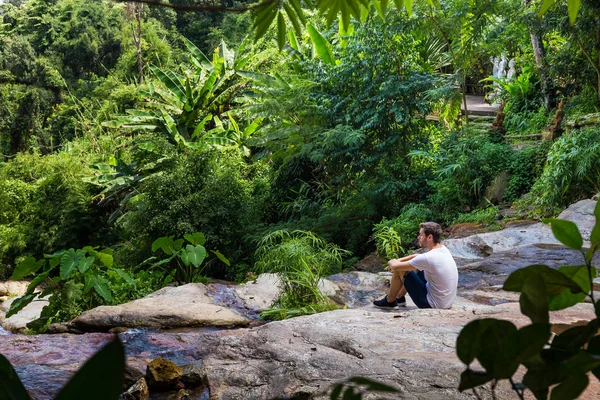 Chiang Mai Tayland ormanda bir şelale üzerinde oturan genç adam