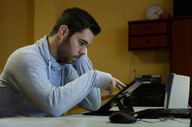 Genç adam cep telefonunu kullanarak tablet, dizüstü bilgisayar ve kulaklıklar