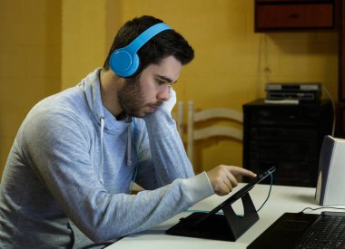 Genç adam cep telefonunu kullanarak tablet, dizüstü bilgisayar ve kulaklıklar